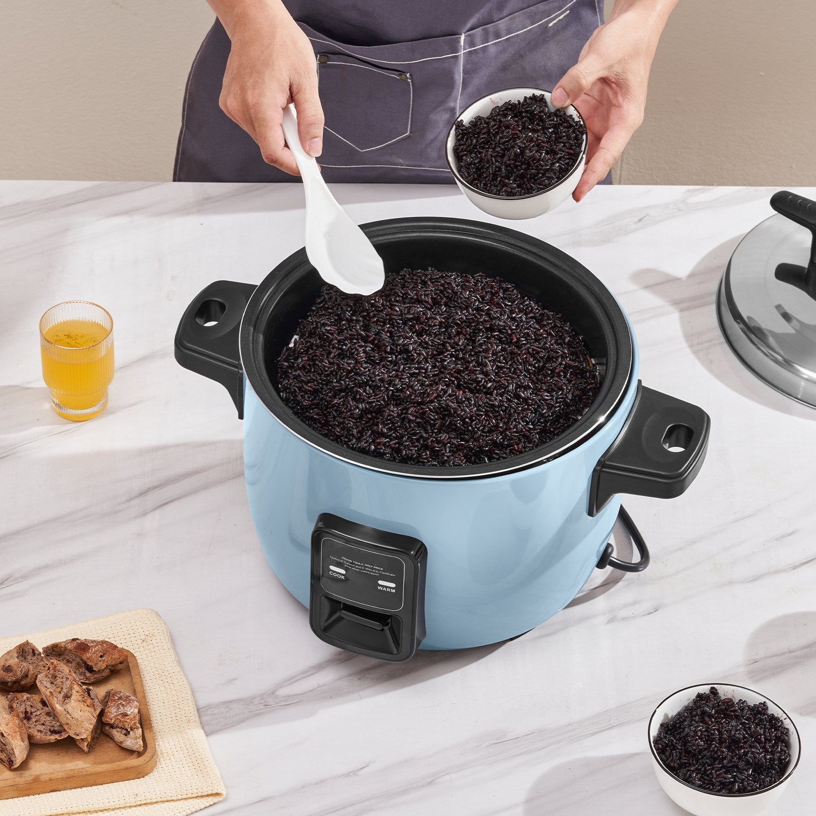 Person adding ingredients to a blue rice cooker on a marble countertop.